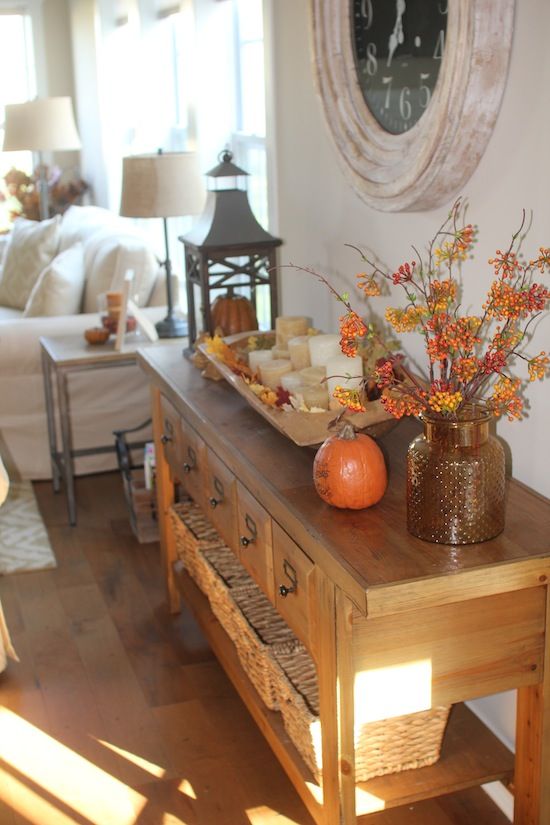 a console table with a fall leaf arrangement, a pumpkin and a wooden bowl with leaves and candles for the fall