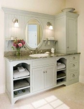 a pastel farmhouse bathroom shows off a large green grey unit that is a vanity and a storage piece at the same time