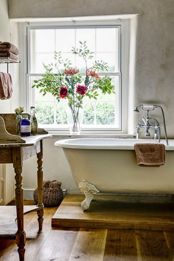 a vintage farmhouse bathroom with a clawfoot bathtub on a platform and a vintage vanity