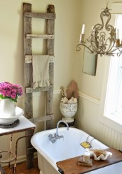 a neutral warm-colored farmhouse bathroom with sandy walls, white beadboard, a clawfoot bathtub and an old ladder to hang towels
