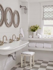 a white vintage farmhouse bathroom with wood frame round mirrors, a large sink, mosaic tiles and a window