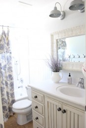 a neutral farmhouse bathroom with a creamy wooden vanity, a vintage frame mirror and a floral print shower curtain