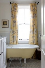 a small farmhouse bathroom with a white vanity, a yellow clawfoot bathtub, yellow printed curtains