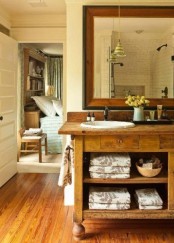 a chic farmhouse bathroom with much rich-stained wood in decor, a large vintage vanity and a large mirror