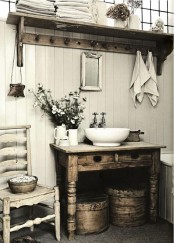 a shabby chic farmhouse bathroom with white plank walls, shabby wooden furniture, a vintage chair and round wooden boxes for storage