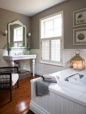 a welcoming farmhouse bathroom with white and grey walls done with beadboard, a bathtub clad with beadboard and a vintage vanity and mirror