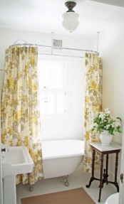 a small farmhouse bathroom with yellow printed curtains, a vintage sink and clawfoot bathtub
