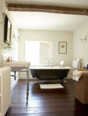 a cozy farmhouse bathroom with a dark wooden floor, a black clawfoot bathtub, a white sink and a mirror