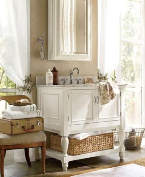 a white vintage farmhouse bathroom with a refined white vanity, white curtains and a chair with suitcases