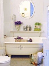 a cute farmhouse bathroom in creamy shades, a clawfoot bathtub, a rug, a shelf with potted plants and a round mirror
