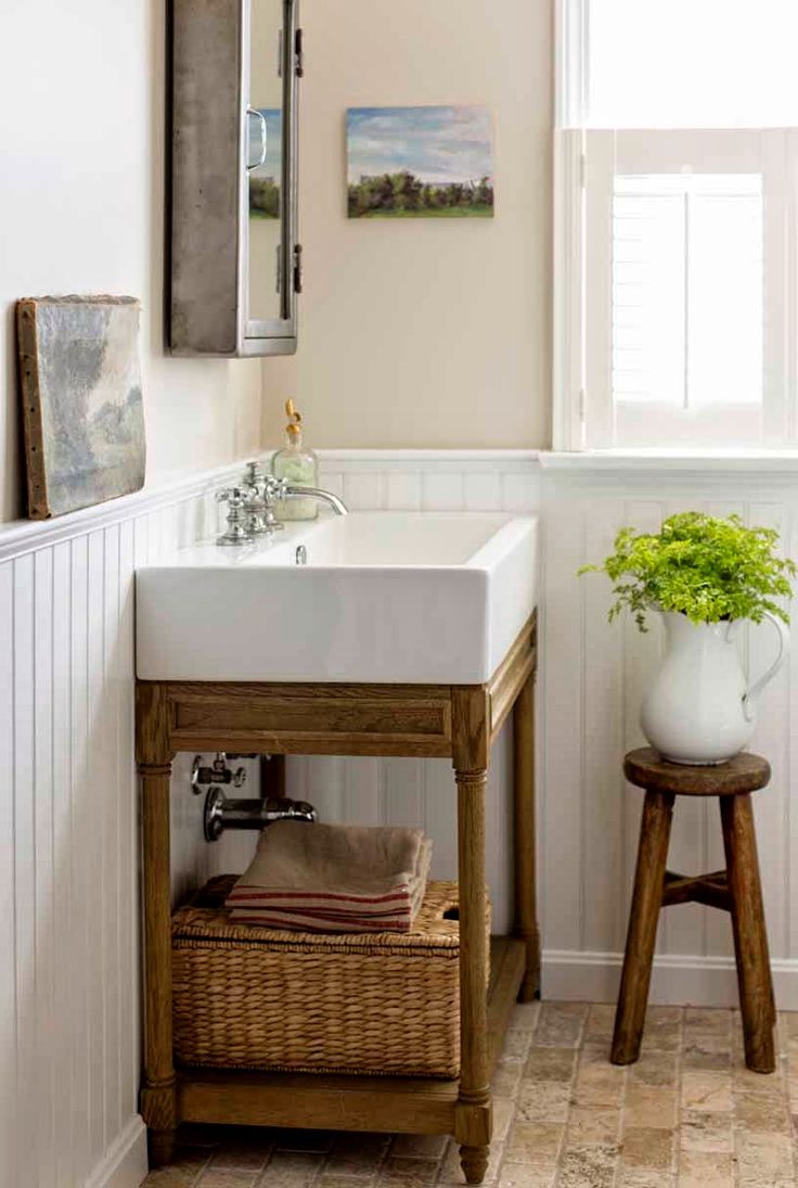 an inviting farmhouse bathroom nook with a wooden vanity, baskets, stools and artworks