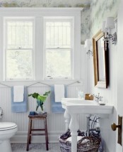 a stylish farmhouse bathroom with printed wallpaper, white beadboard, a sink and a mirror in a vintage frame