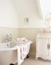 a cute and welcoming farmhouse bathroom in creamy and off-white, a blush bethtub, off-white beadboard and a vintage vanity