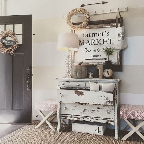 a shabby chic dresser, upholstered stools, a jute rug, a rack with hooks and a lamp plus some wreaths