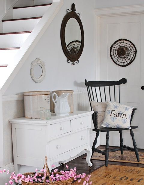 a white vintage sideboard, a black vintage chair, a round mirror and tin cans for storage plus a FARM pillow