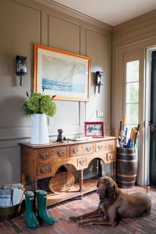 a vintage farmhouse entryway with a large refined console, a brick floor, a seascape and a jug with green hydrangeas