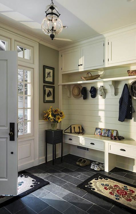 a farmhouse entryway with an ivory wooden furniture piece iwth a built-in bench of drawers and more storage space plus dark tiles on the floor for a contrast