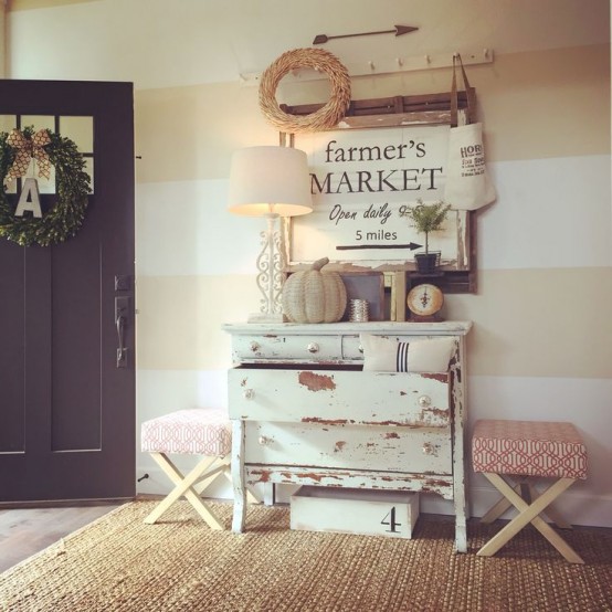 a shabby chic meets farmhouse entryway with a white dresser, wreaths, pumpkins and a large artwork