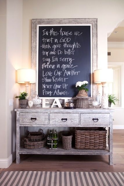 a weathered wood console table with drawers, a striped rug, baskets for storage, lamps and a framed chalkboard sign