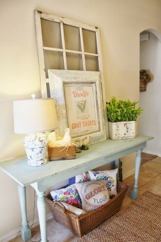 a light blue console, a table lamp, a basket with pillows, an artwork and planted greenery plus a jute rug