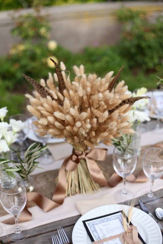 a beautiful wheat and feather arrangement with a silk ribbon is a chic rustic centerpiece