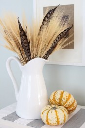 a white jug with wheat, feathers and mini pumpkins is a nice fall arrangement and centerpiece
