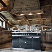 a rustic chalet kitchen all clad with reclaimed wood, with a large vintage kitchen island and built-in lights looks welcoming and cozy