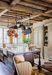 a neutral traditional kitchen with chalet touches – a wooden ceiling with beams, a dark stained kitchen island and pans hanging over the kitchen island