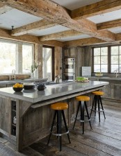 a traditional chalet kitchen clad with reclaimed wood, with wooden beams on the ceiling, with stone countertops and bright stools for a bold touch