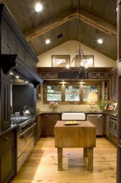 a cozy chalet kitchen with white stone walls, dark cabinets and a hood, a wooden kitchen island and built-in lights