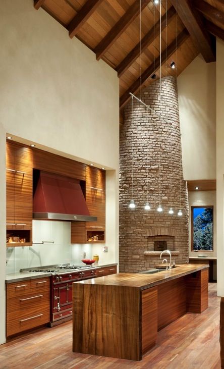 a modern chalet kitchen done with a stone clad hearth and stove, with wooden furniture and a red cooker plus pendant lamps
