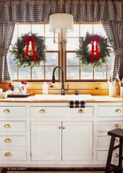 a buffalo check curtain and towel, evergreen wreaths with red bows bring a Christmas feel to the space