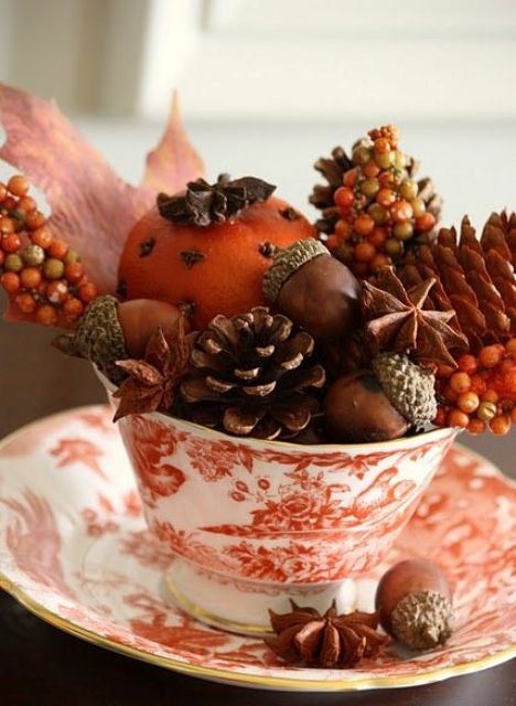 a vintage printed teacup filled with nuts, pinecones, fall leaves and berries and a pomander