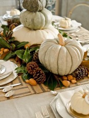 a stylish Thanksgiving centerpiece of pinecones, nuts, foliage and oversized neutral pumpkins stacked