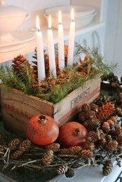 a rustic centerpiece of a crate with evergreens and pinecones plus candles and pinecones and pomegranates around