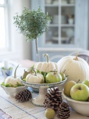 a cute fall centerpiece of a porcelain stand with foliage, pumpkins, apples and pears for a harvest touch