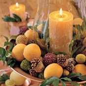 a chic Thanksgivign party centerpiece of a metal tray filled with pinecones, fruits, pea balls and foliage plus a large candle in the center