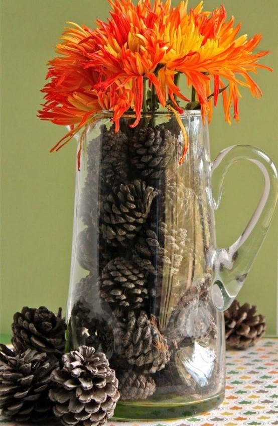 a simple clear glass jug filled with pinecones and topped with bright fiery red blooms for a fall-inspired space