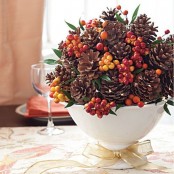 a luxurious Thanksgiving centerpiece of a white bowl with pinecones, berries, foliage and with a playful gold bow