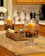 a casual fall centerpiece of a wooden tray filled with pinecones and bulbs, with vases with pinecones and nuts plus candles next to it