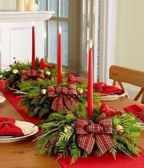a red table runner, evergreen and red berry arrangements with red plaid bows and red candles dress up the table for Christmas and give it a bright holiday look