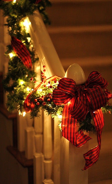 an evergreen and light garland with red berries and a red plaid bow is a cool way to style railing, a mantel or window