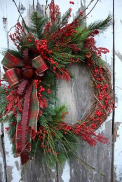 a vine wreath with evergreens, red berries, a moody plaid box and bells is a lovely idea for a Christmas front door