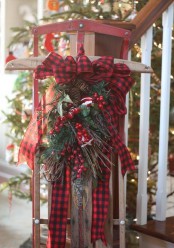 a vintage sleigh with evergreens, twigs, berries, bells and a large red plaid bow on top is a cool and pretty decoration for outdoors