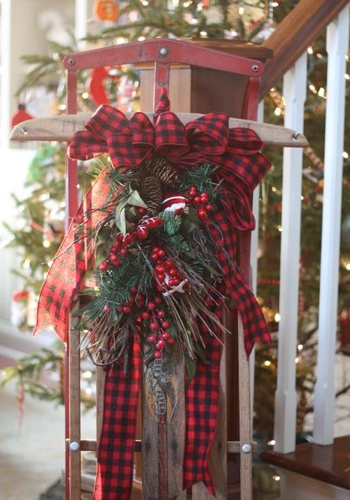 a vintage sleigh with evergreens, twigs, berries, bells and a large red plaid bow on top is a cool and pretty decoration for outdoors