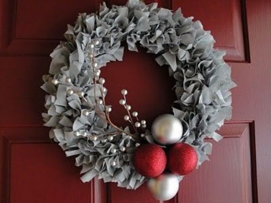 a red door with a grey fabric wreath, with silver and red ornaments and twigs with berries are amazing for Christmas decor