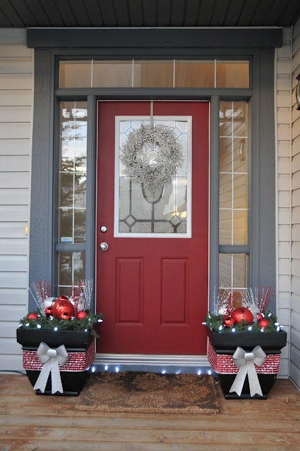 an entrance with a red door and grey windows, black planters with grey and red ornaments and twigs is a cool idea for modern Christmas styling