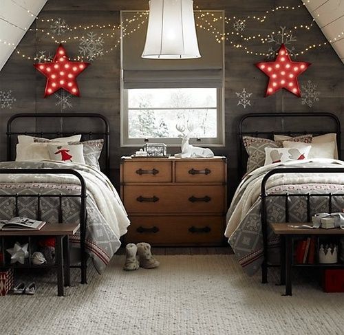 a grey reclaimed wood accent wall with red marquee stars, lights and red and grey Christmas-themed bedding
