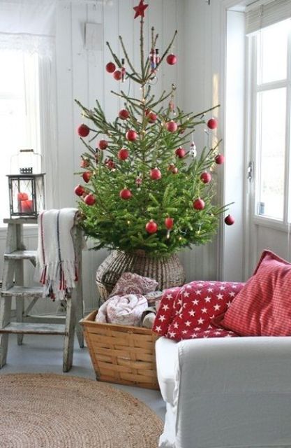 a Christmas tree in a basket with red ornaments all over, a basket with blankets and red printed pillows on the chair is a cool idea