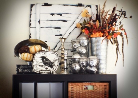 a rustic console table with a crow plate, pumpkins, a bold feather, greenery and bloom arrangement and silver covered fruits and veggies